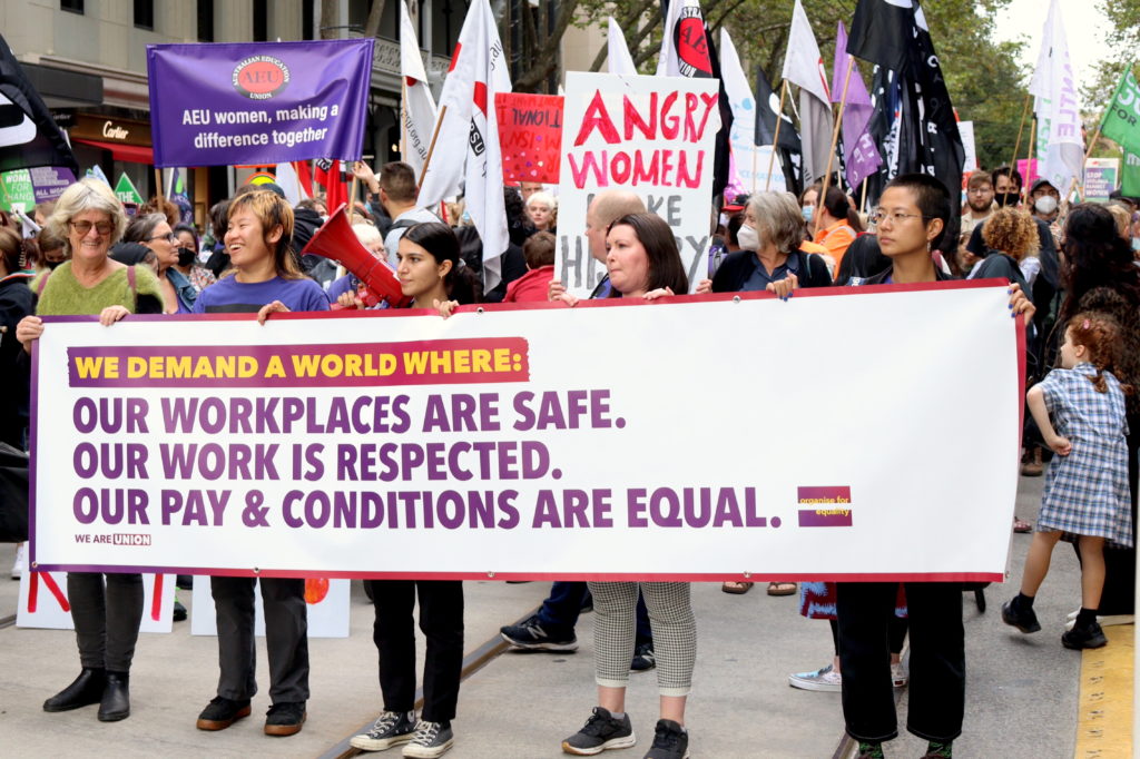 Unionists at an International Women's Day march hold a banner that reads:

We demand a world where
Our workplaces are safe.
Our work is respected.
Our pay conditions are equal. 
