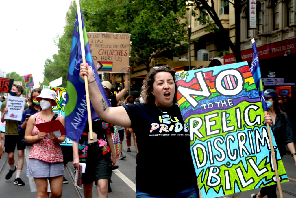 An IEU member from the Victorian / Tasmanian branch marches with banners and a vibrant sign that reads: "No to the relig discrim bill".