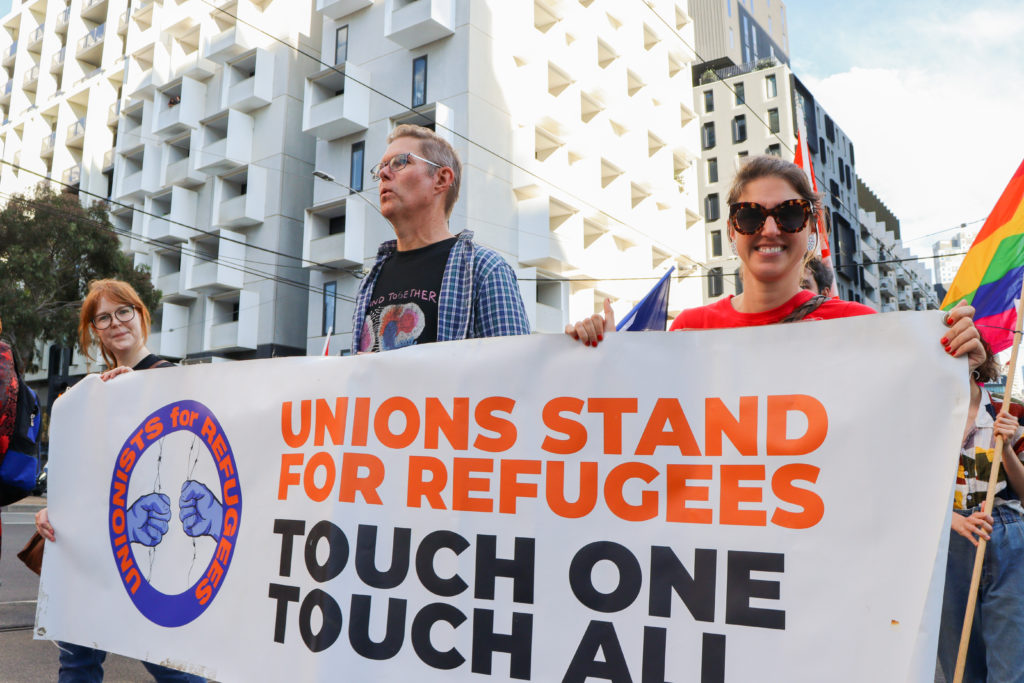 Union members carry a banner that reads 'Unions stand for refugees. Touch one touch all'. 