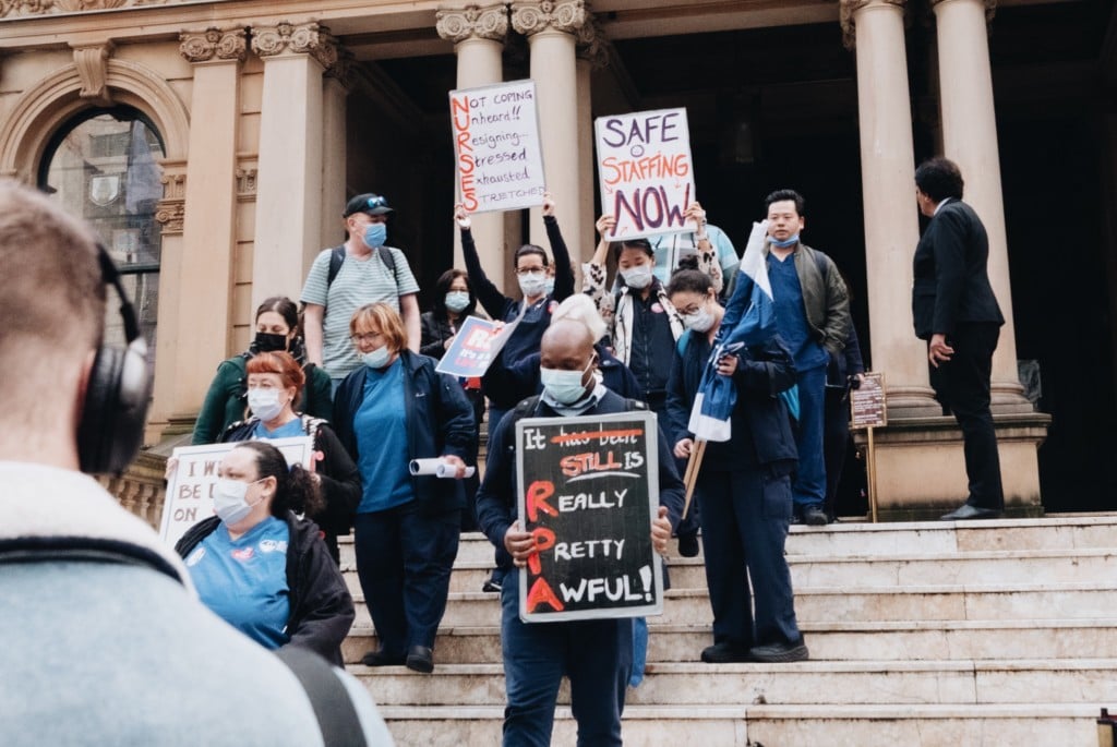 Striking unionised nurses walk down the steps of NSW parliament with placards in hand