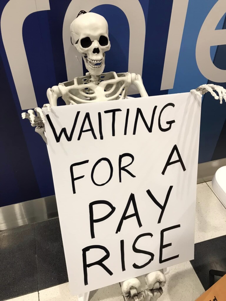 A sitting model skeleton 'holding' a sign that reads: waiting for a pay rise.